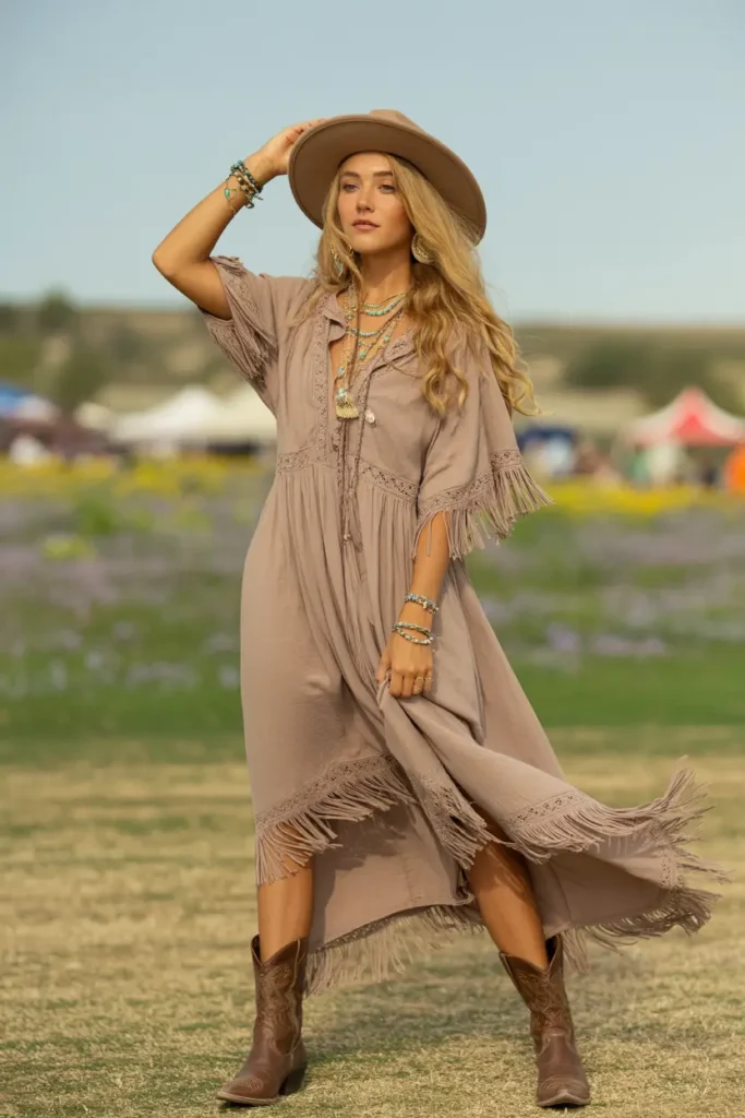 Young woman in a flowing fringe maxi dress, turquoise jewelry, wide-brim hat, and brown leather cowboy boots styled in bohemian festival Cowboy Boots Outfits at golden hour